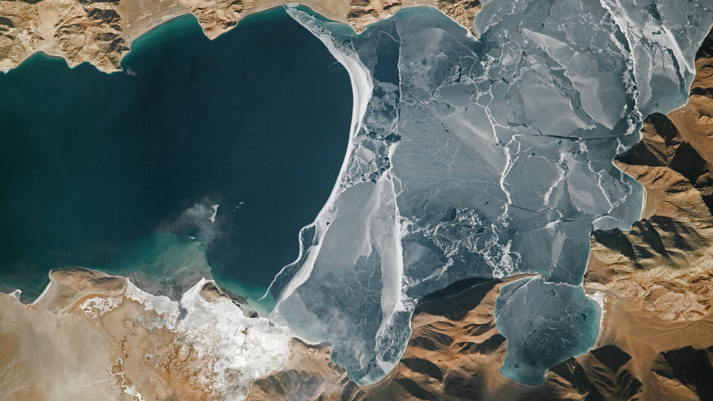 An astronaut photo of a section of a lake half covered in fracturing ice