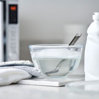 a mixing bowl with water with washing up liquid on a worktop with a microwave in the background