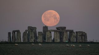 the full moon hangs in the sky above a monument consisting of stacked rock slabs