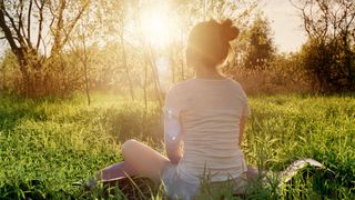 Young woman sitting in yoga position enjoying sunset in nature