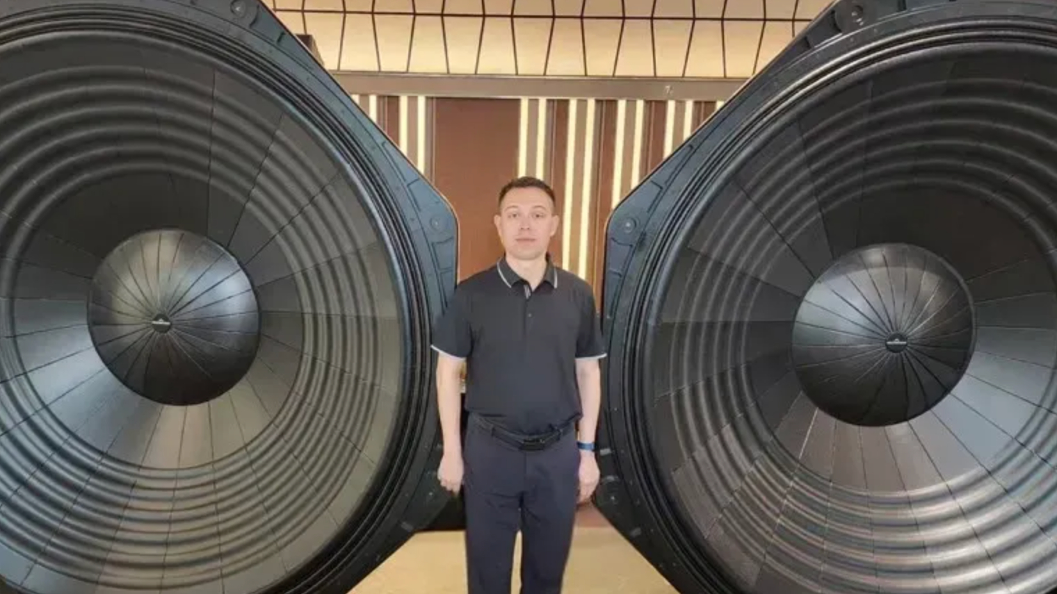 A man dwarfed by two huge sub woofer speakers