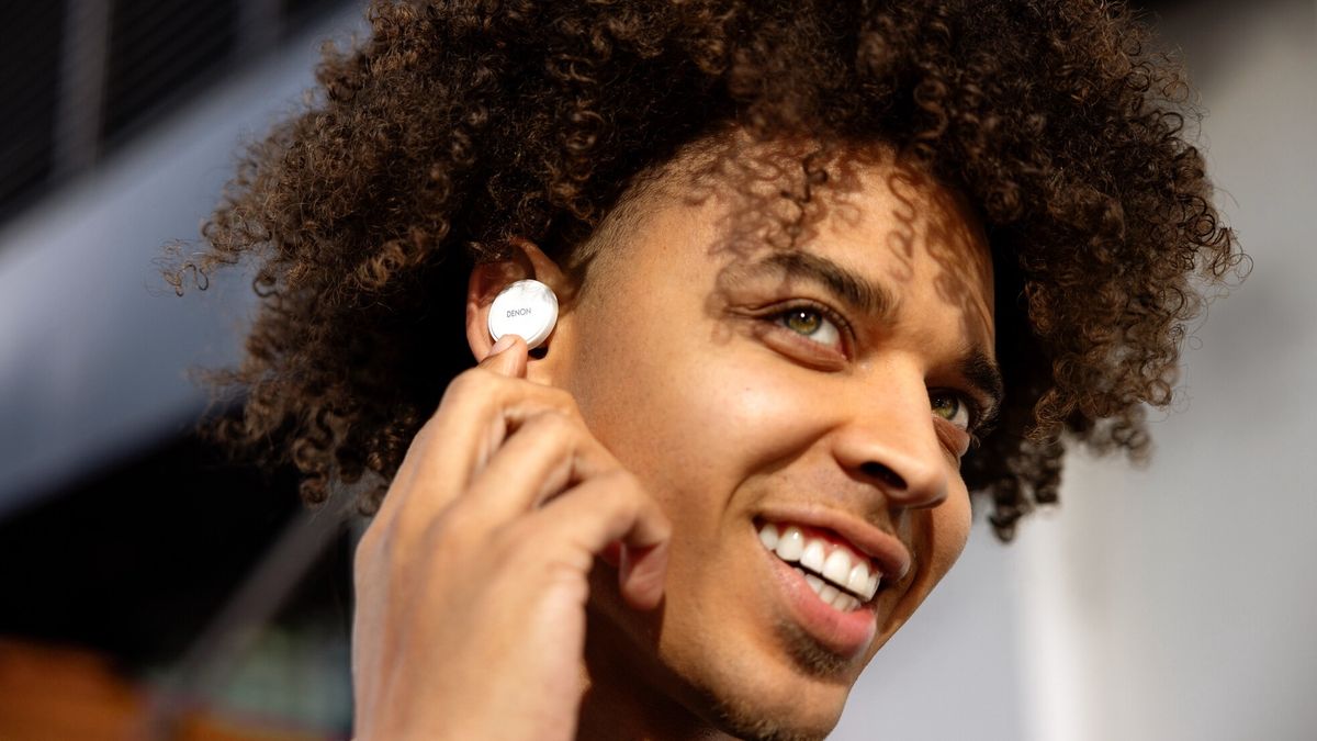 A young man wearing the Denon PerL wireless earbuds and smiling