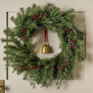 Real Touch Red Berry and Pine Wreath against a cream wall.