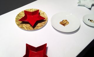 Two plates, a white one with sauce in the middle and a gold one with a red star shaped bowl on top of it.