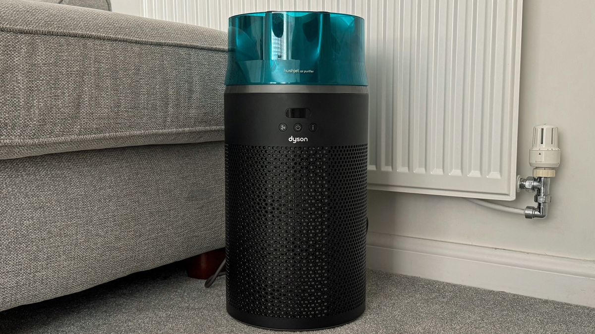 Dyson HushJet air purifier placed on a carpeted living room floor beside a sofa and radiator