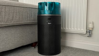 Dyson HushJet air purifier placed on a carpeted living room floor beside a sofa and radiator