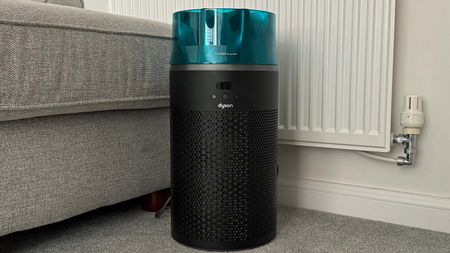 Dyson HushJet air purifier placed on a carpeted living room floor beside a sofa and radiator