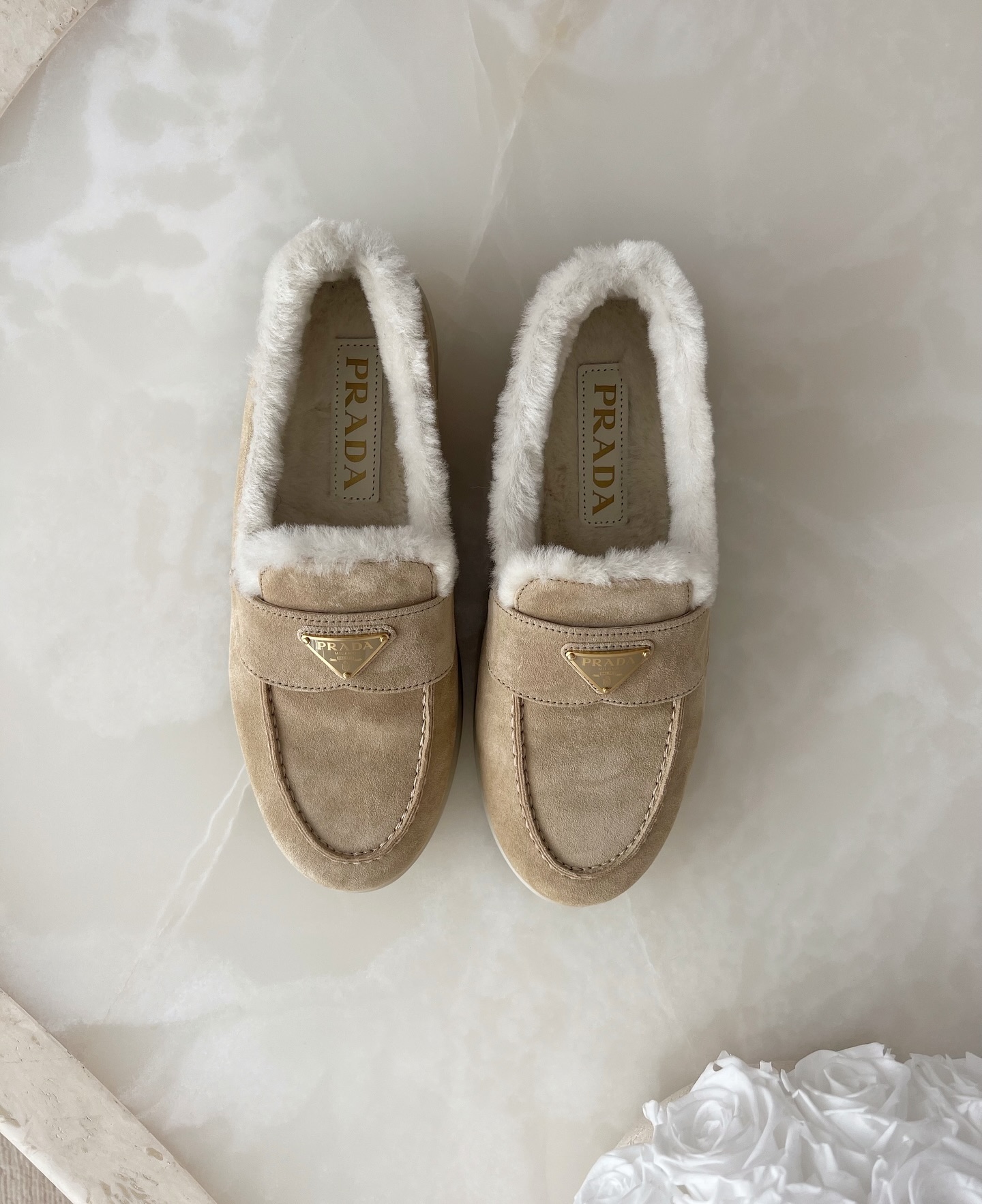 @lovisabarkman showcases a pair of beige suede shearling loafers from Prada on a marble surface