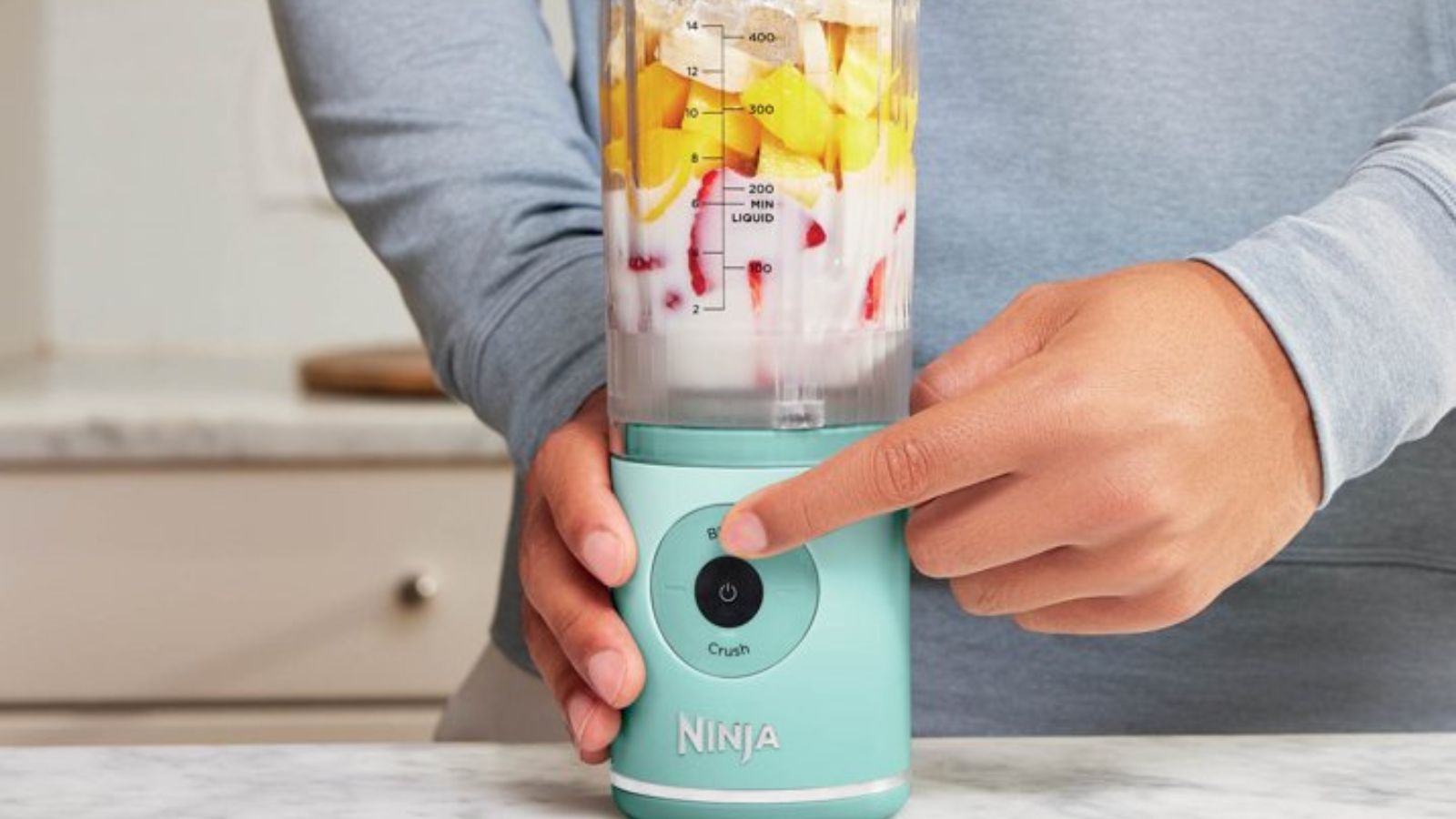 A man switching on the mint colored Ninja Blast Max blender, filled with tropical ingredients