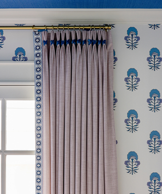 Close up of a grey curtain with blue detail and blue wallpaper print