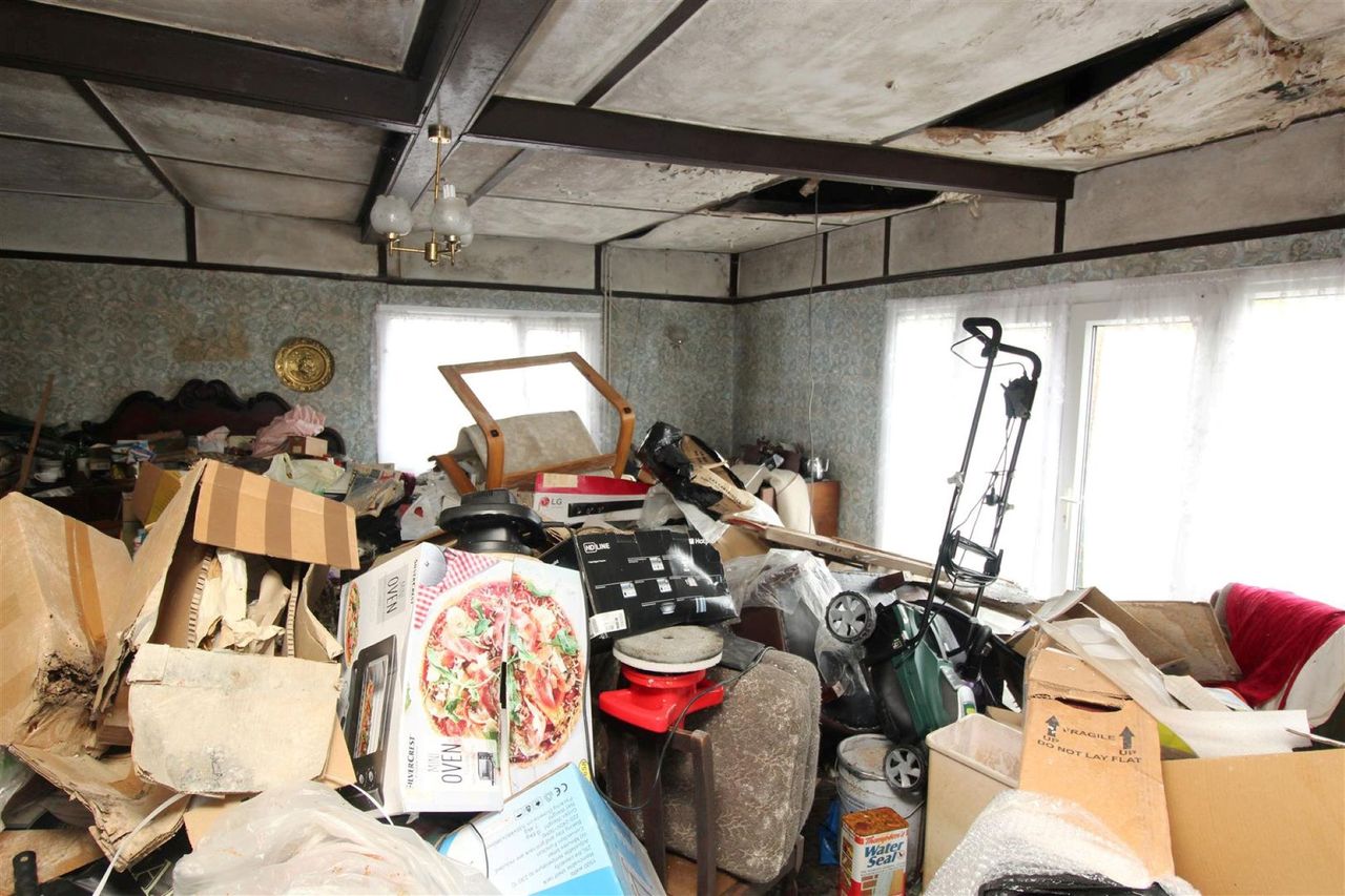 A garage piled high with rubbish with a lawnmower witting on top