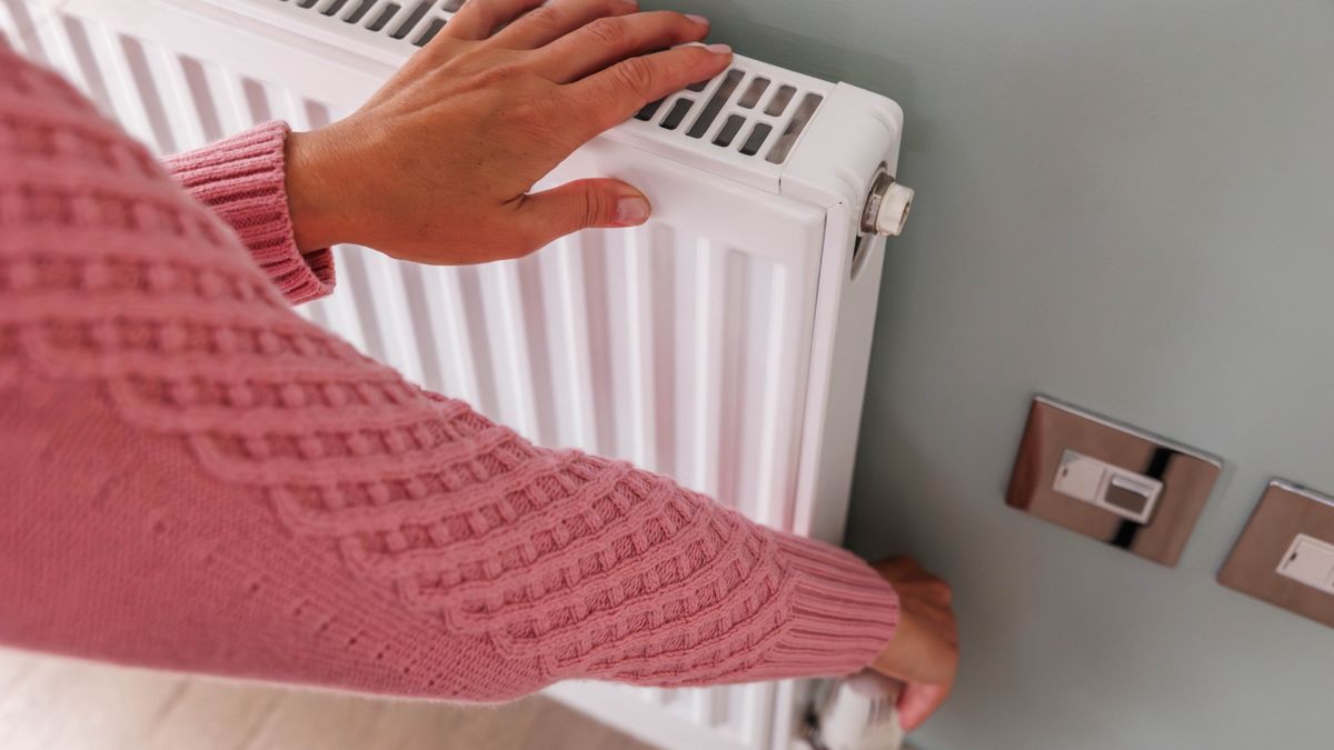 person in pink jumper touching white radiator and adjusting valve