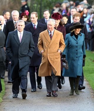 Prince Andrew walking. next to King Charles and Queen Camilla on Christmas Day with his hands in his pockets and a long coat