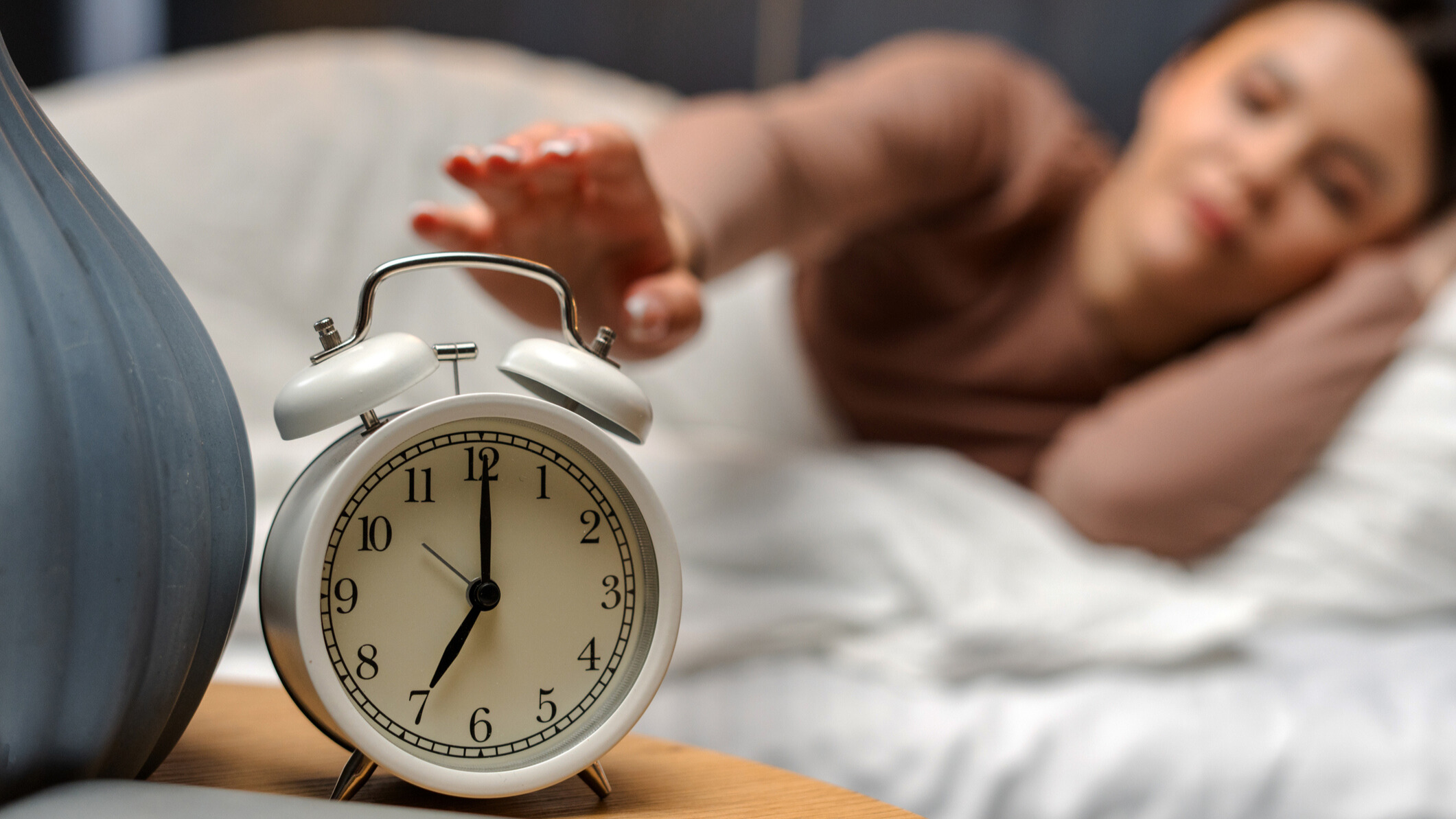 Woman about to hit snooze on an alarm clock placed on the side table