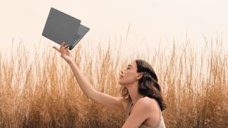 A woman holding up an Asus laptop in a field of wheat