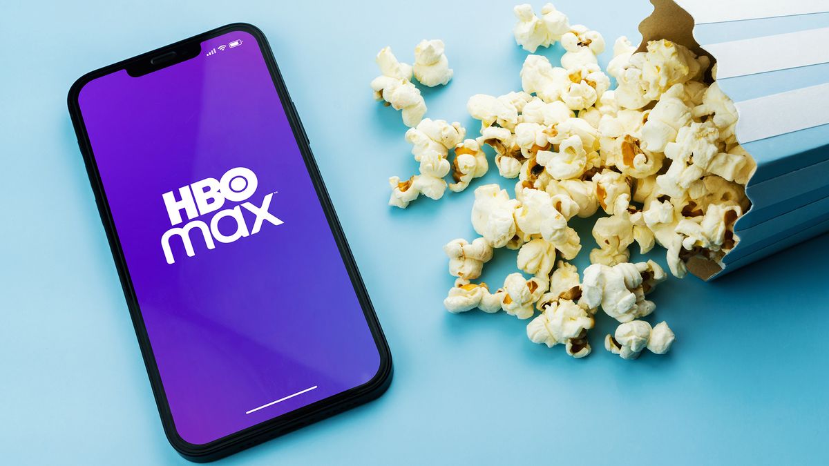 A phone with the HBO Max logo sits to the left of a spilled popcorn container