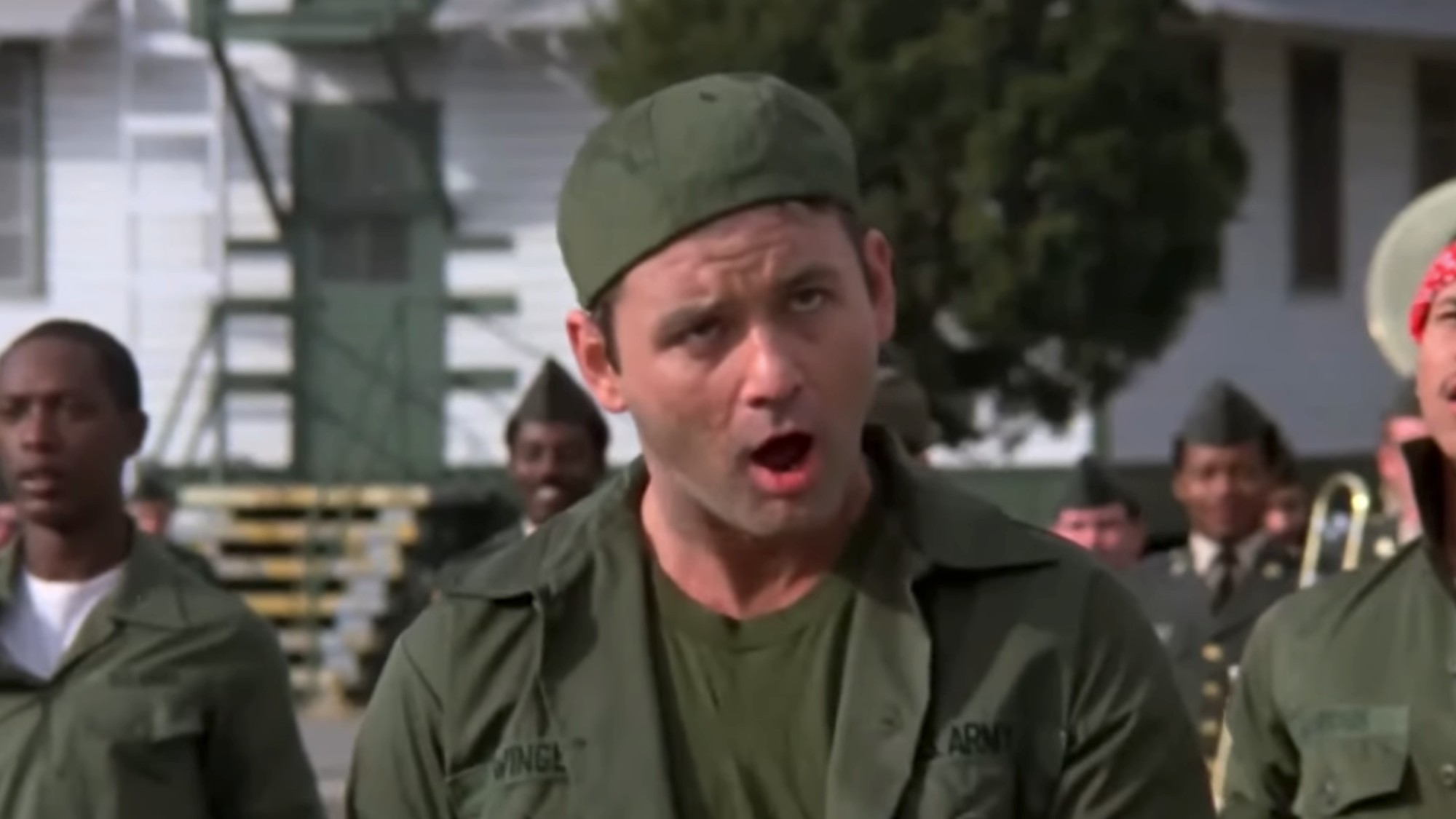 Bill Murray making a funny face in army fatigues and a backwards cap in Stripes. 