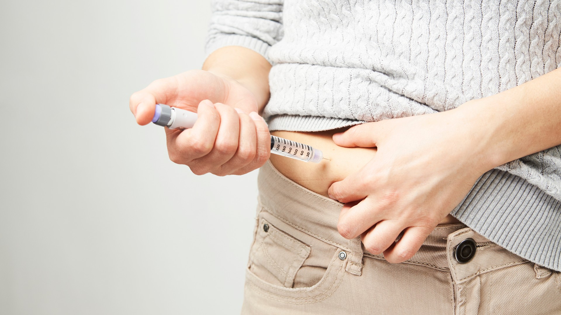 Young woman doing insulin injection pen, close-up. Gecko Studio via Shutterstock