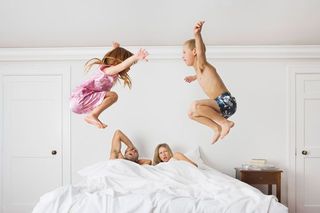 Children jumping on a bed with their parents still in it.