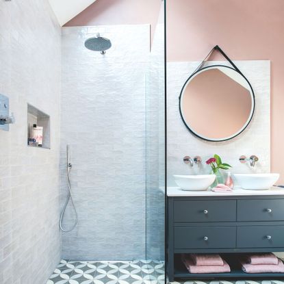 Bathroom with pink walls and white tiles, a walk-in shower on the left and a double sink vanity with mirror above on the right