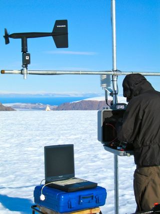 Canadian researcher maintaining one of several weather station on the Devon Island, Nunavut, Canada. The researchers camp can be seen in the foreground. Monitoring the meteorological conditions over the ice cap helps researchers to determine glacier respo