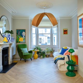 Light wood chevron style parquet flooring in a cream living room with white sofa and green velvet armchair