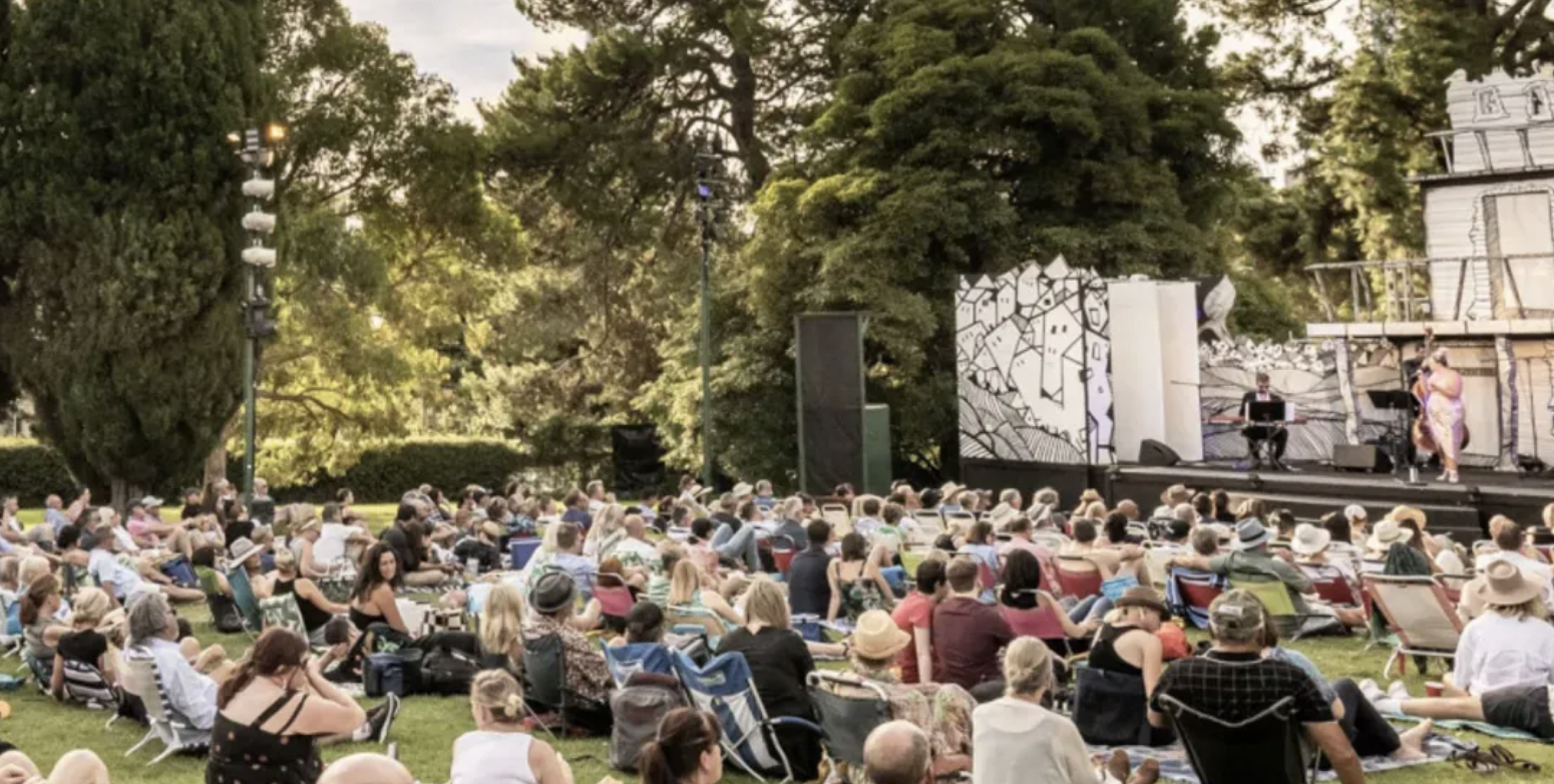 an image of some open air theatre at Kew Gardens whilst people sit on the grass watching