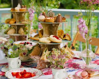 A pop up cake stand on an outdoor table with cakes, pastries and cut flower displays