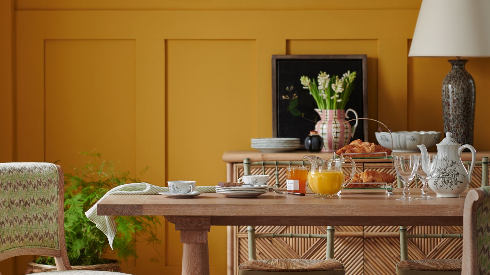 A yellow dining room with a light wooden table covered in breakfast items. 