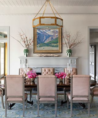 neutral dining room with pink leather dining chairs, large wooden table, blue patterned rug and fireplace