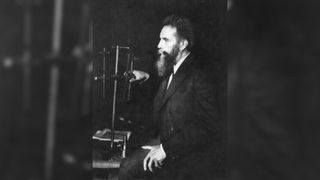 A man with a beard sits in front of an apparatus made of metal