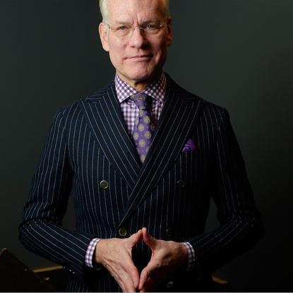Man neatly dressed in a pinstripe suit and purple check shirt with purple tie