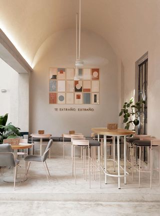 Extraño cafe with high arched ceiling wooden tables and pale pink and grey chairs and stools