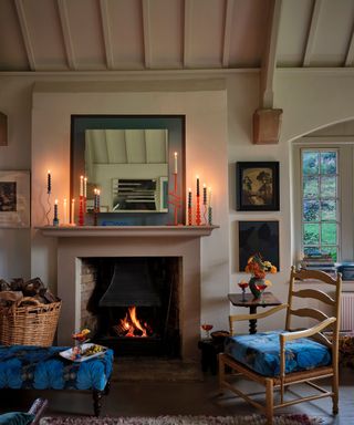 cozy living room with neutral walls, vintage furniture and mantel with lots of tall candles and square mirror with blue and black painted border