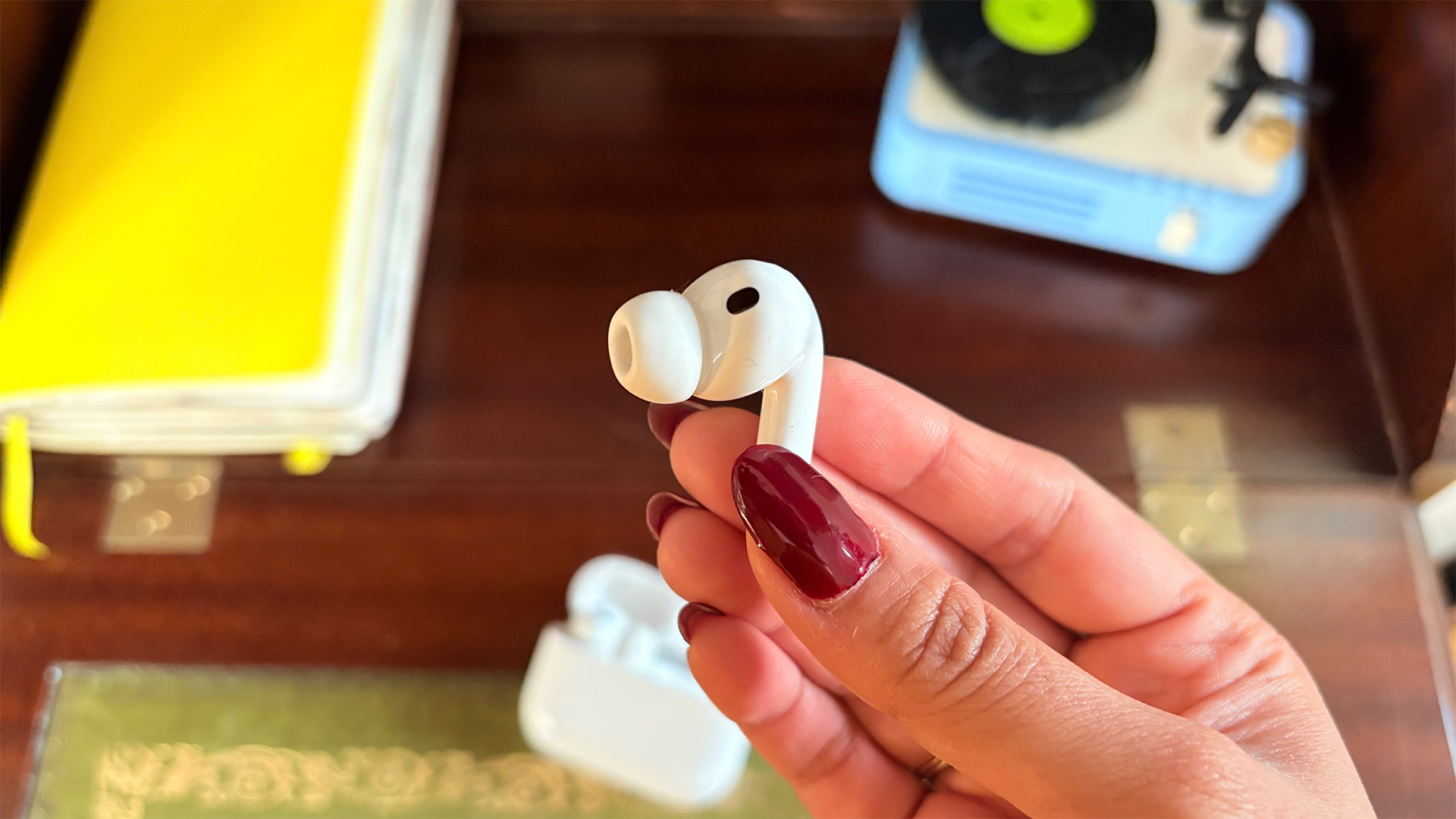 Apple AirPods Pro 3 wireless earbuds, one earbud held between fingers and thumb above desk