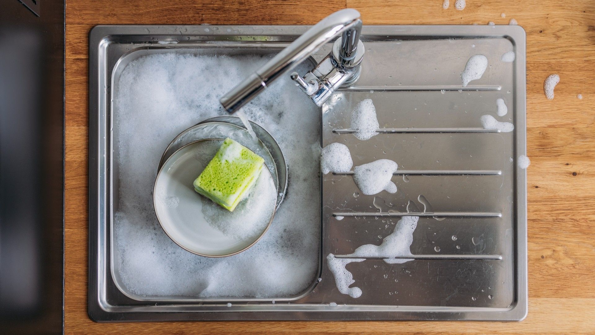 birds eye view of a sink full of hot soapy water, with dishes and a sponge in it