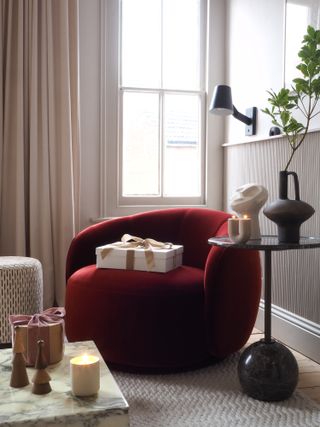 A dark red armchair with a present on top and black side table with vase