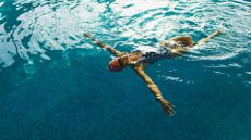 Woman lying on her back wearing goggles and cap, doing swimming workouts in pool