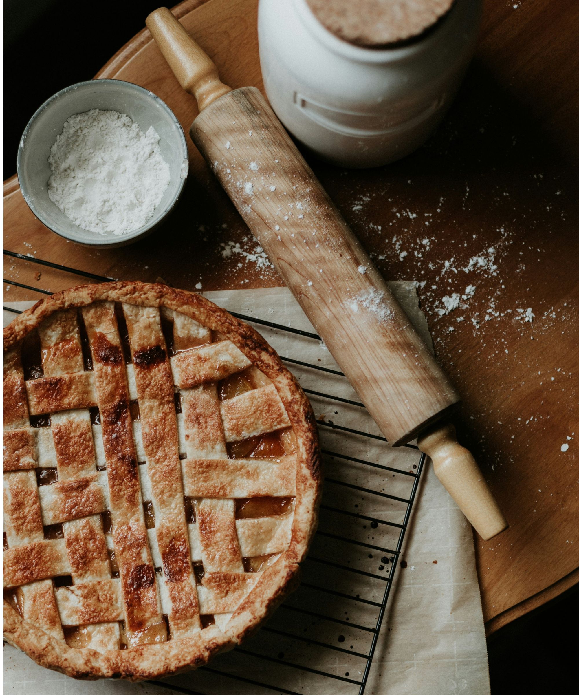 Sweet pie on cooling rack next to rolling pin and bowl of flour