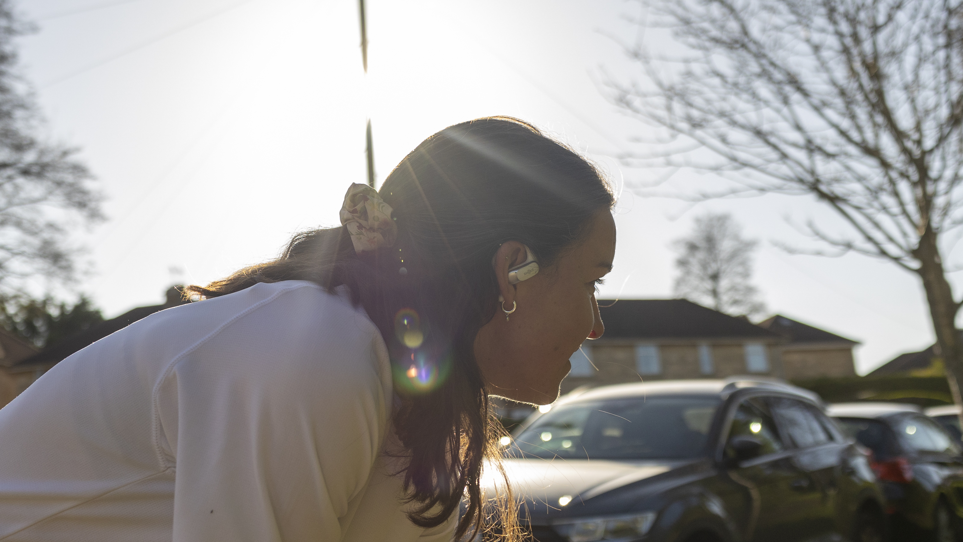A side view of a female wearing the Shokz OpenFit Air headphones in bright sunshine