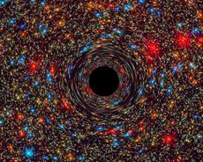 Here, a computer-simulated image of a supermassive black hole at the core of a galaxy, with the black region at the center representing the event horizon.