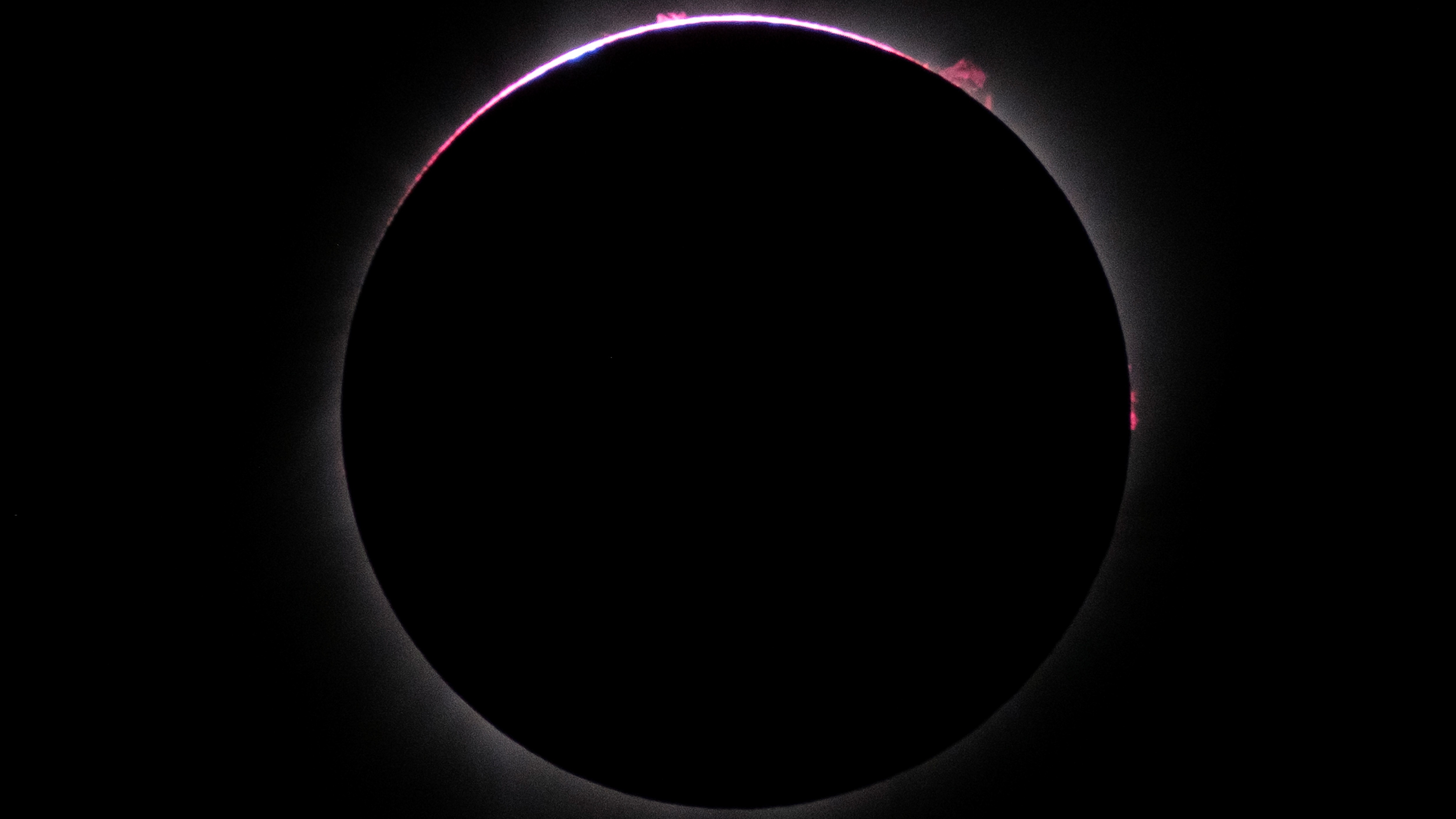 close up view of the sun completely blocked by the moon, there is a distinct pink outline especially around the top of the eclipse.
