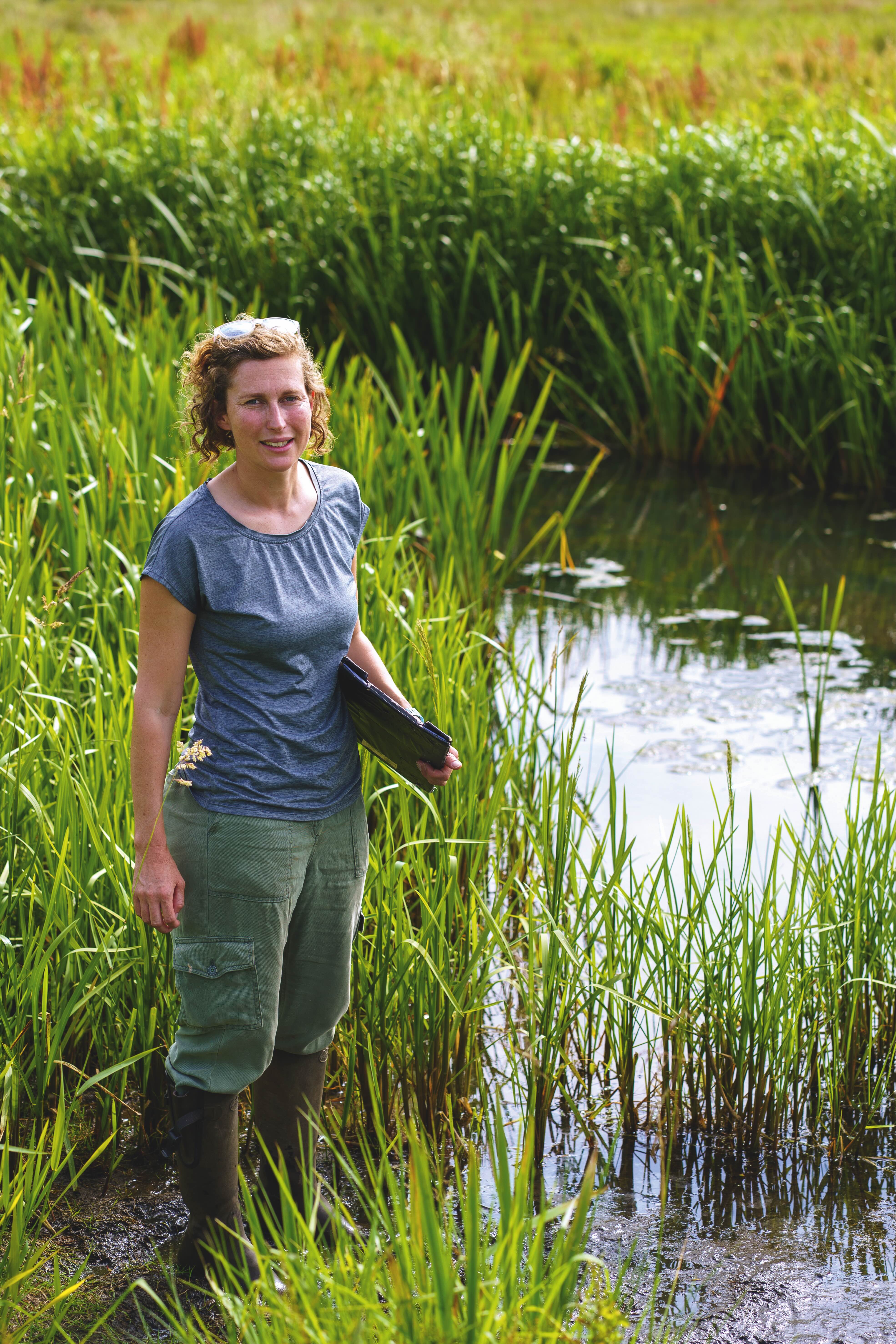 Lizzie Grayshon stands in some reeds looking at the camera holding a clipboard