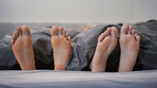 Two pairs of feet sticking out from under a duvet