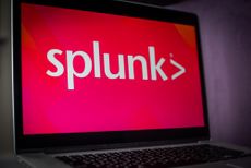 Splunk logo on a laptop with a bright pink background in a dark room