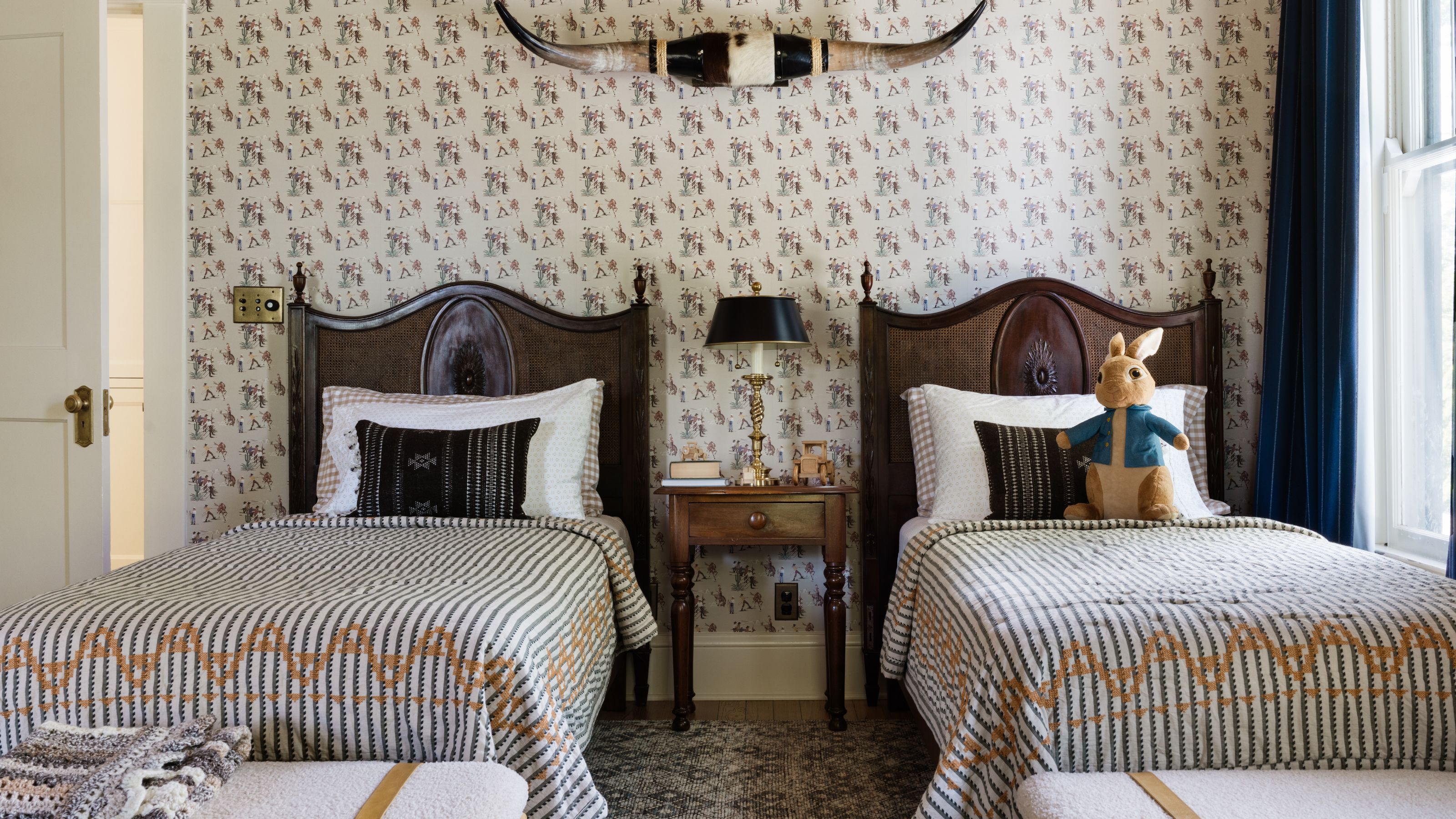 a boys twin bedroom with two wooden beds, striped linens, patterned wallpapered and a Peter Rabbit toy