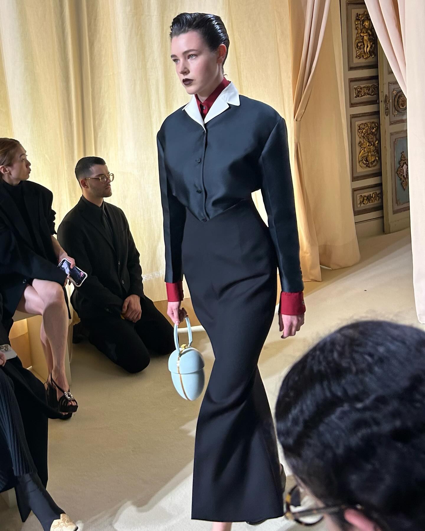 Photo of a Bally model wearing a satin blazer tucked into a black column skirt from the FW24 collection.