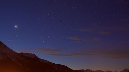 A view of a deep purple night sky with a red glowing mountain range underneath a series of twinkling stars.