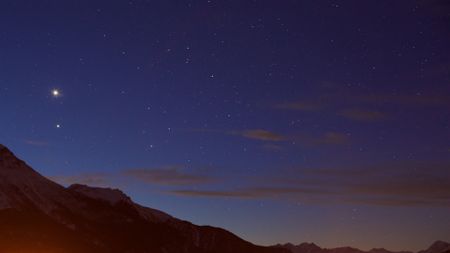 A view of a deep purple night sky with a red glowing mountain range underneath a series of twinkling stars.