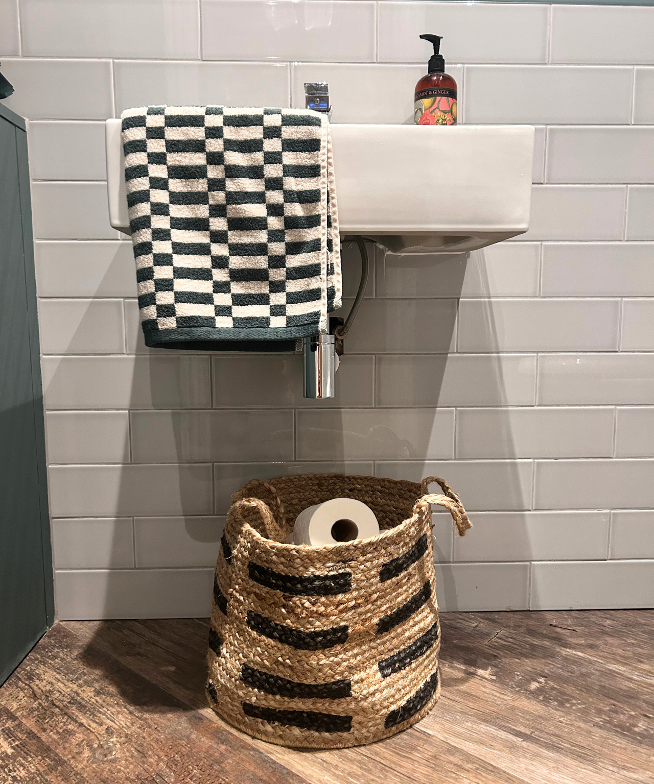 Gray and green bathroom with basket full of toilet rolls and green checked towel hanging over a sink